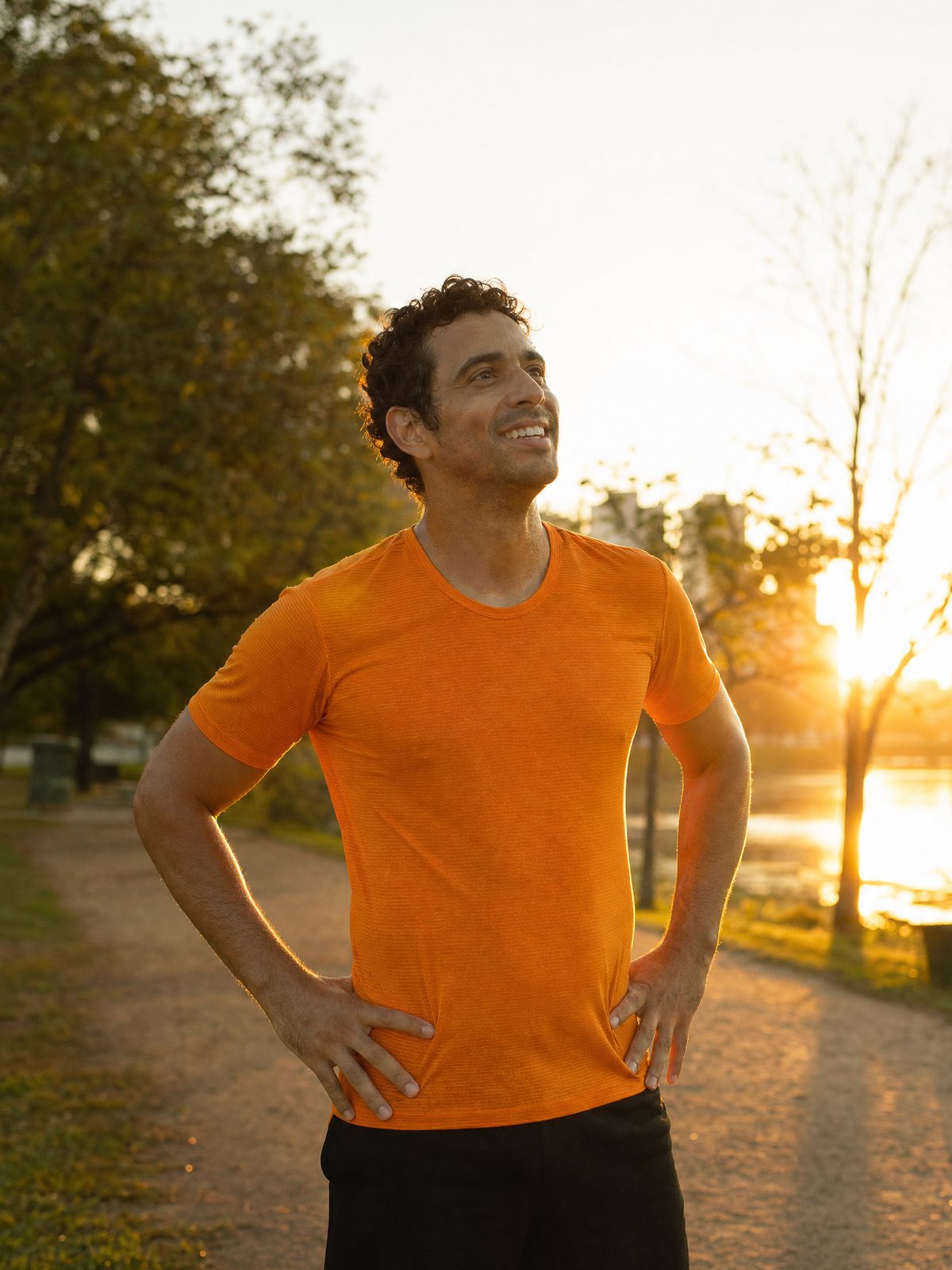 Corredor amador para ao fim do treino e olha o nascer do sol com as mãos na cintura.