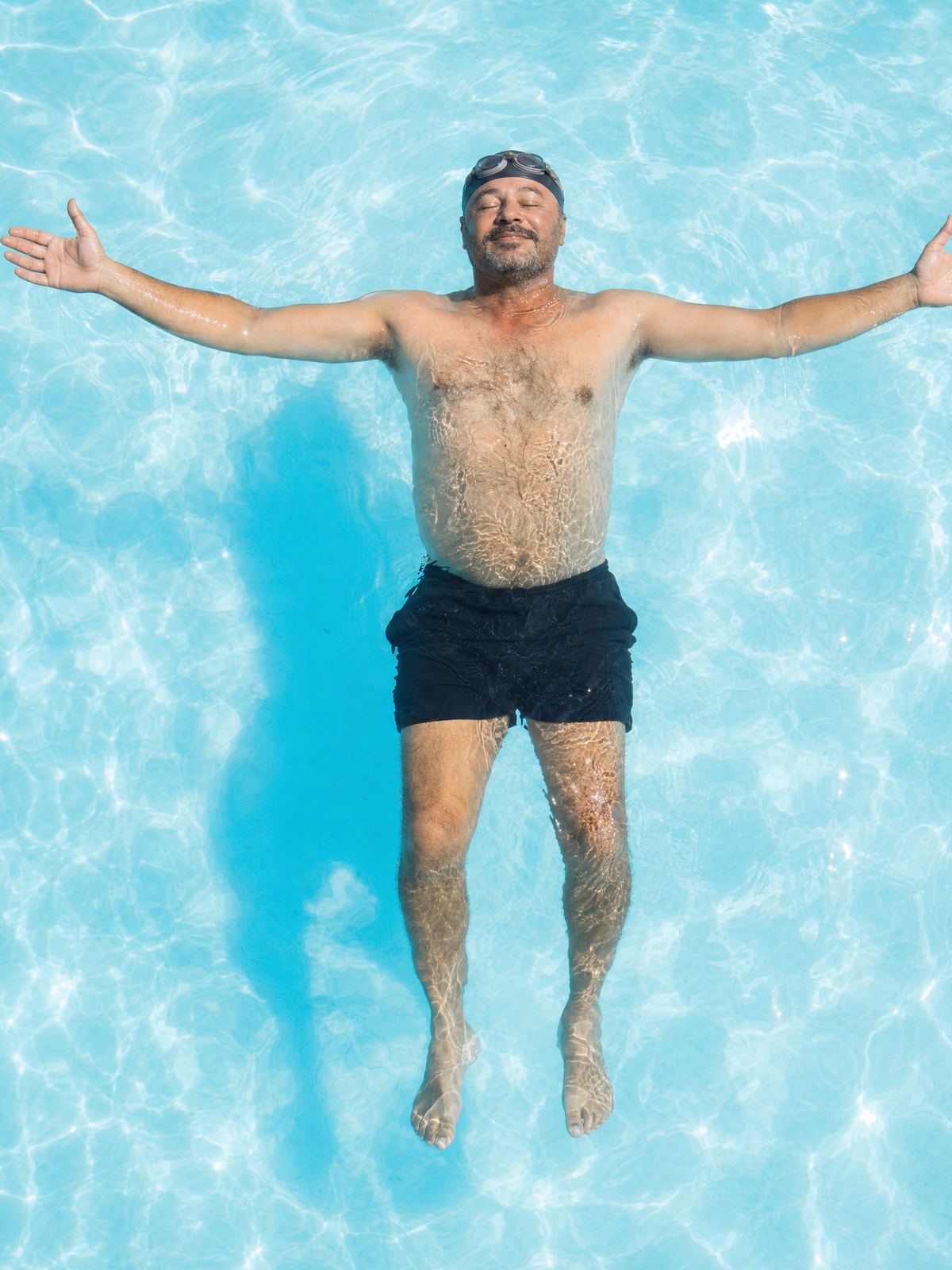 Homem boia de costas com os braços abertos em uma piscina de água azul-clara.