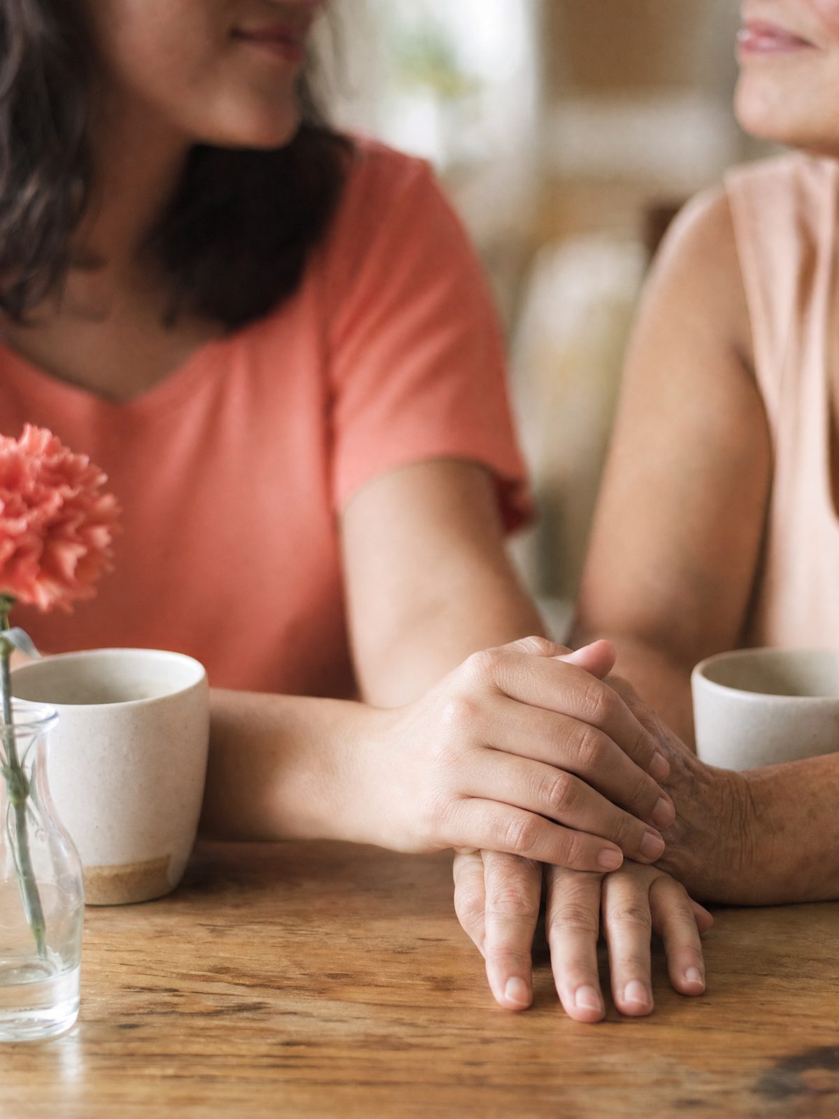 Duas mãos de gerações diferentes se tocam sobre a mesa, ao lado de xícaras de café.